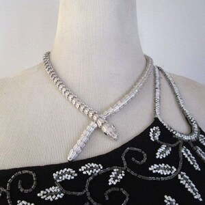 Op de afbeelding: Een zilveren slangenketting met een slangenkop-hanger. De ketting is op een mannequin die een zwart, met kralen bezet topje draagt.