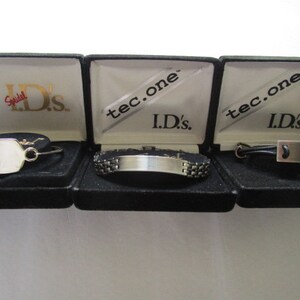 May include: Three black boxes with silver bracelets inside. The boxes are labeled "ID's" and "tec.one".