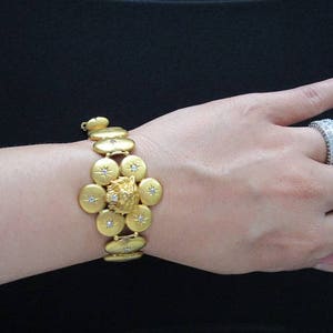 May include: A gold bracelet featuring a lion head charm and small diamonds. The bracelet is made up of multiple round links with a central flower-shaped design.