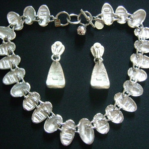 Puede incluir: Un collar de plata con una cadena de eslabones ovalados conectados y pendientes colgantes de plata a juego. El collar tiene un cierre de plata.