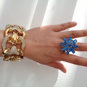May include: A gold bracelet with a chain link design and clear rhinestones. A blue ring with a starburst design and blue rhinestones.