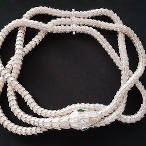 Peut inclure: Un collier de serpent en argent avec un pendentif t&ecirc;te de serpent orn&eacute; de pierres pr&eacute;cieuses vertes pour les yeux. Le collier est compos&eacute; d'une cha&icirc;ne d'&eacute;cailles imbriqu&eacute;es.