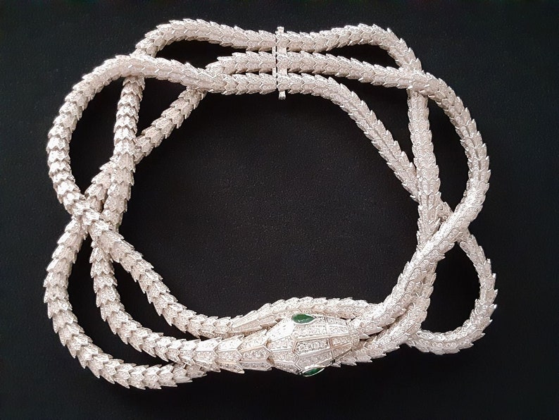 Peut inclure: Un collier de serpent en argent avec un pendentif t&ecirc;te de serpent orn&eacute; de pierres pr&eacute;cieuses vertes pour les yeux. Le collier est compos&eacute; d'une cha&icirc;ne d'&eacute;cailles imbriqu&eacute;es.
