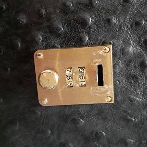 May include: A gold combination lock with a black background. The lock has a dial with the numbers 7, 6, 5, and 4.