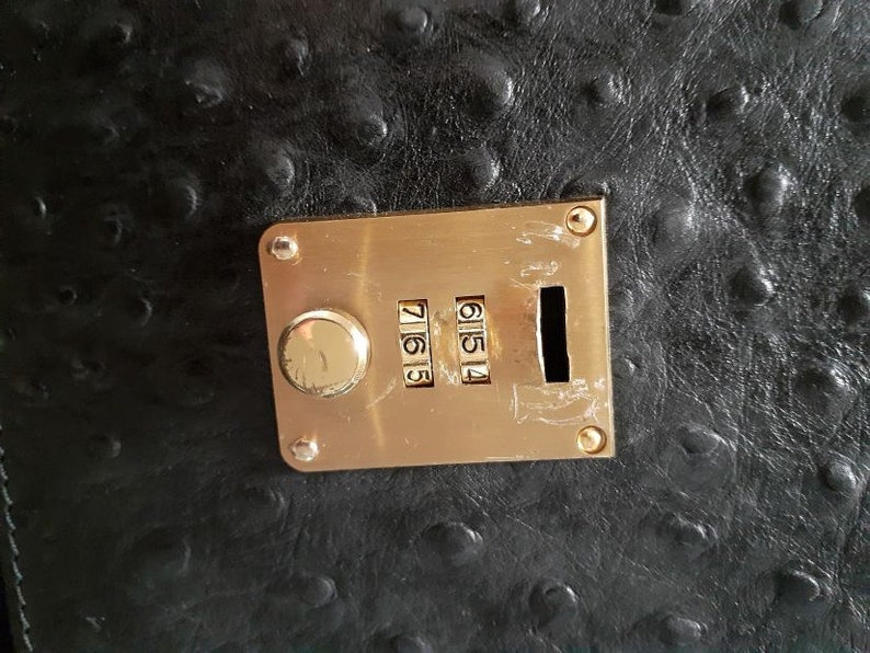 May include: A gold combination lock with a black background. The lock has a dial with the numbers 7, 6, 5, and 4.