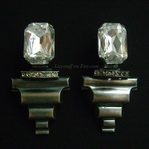 May include: A pair of silver earrings with large, clear, faceted crystal stones. Each stone is set in a silver base with a row of smaller crystals around the base.