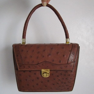 May include: A brown ostrich leather handbag with a gold clasp and top handle.