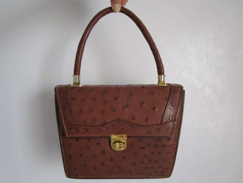 May include: A brown ostrich leather handbag with a gold clasp and top handle.
