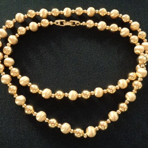 May include: A gold-toned necklace made of round beads. The necklace is double-stranded and has a clasp closure.
