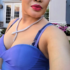Op de afbeelding: Een vrouw draagt een blauwe strapless jurk met een zilveren slangenketting.