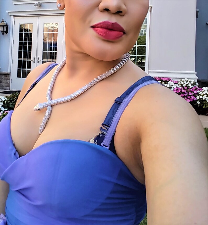 Op de afbeelding: Een vrouw draagt een blauwe strapless jurk met een zilveren slangenketting.