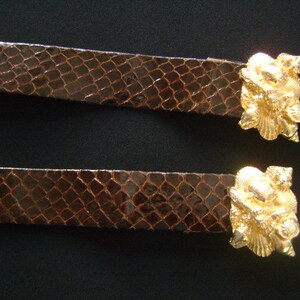 May include: Two brown leather belts with gold-tone shell-shaped buckles. The buckles are detailed with intricate designs.