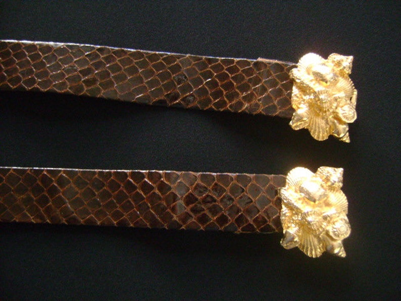 May include: Two brown leather belts with gold-tone shell-shaped buckles. The buckles are detailed with intricate designs.
