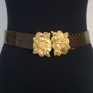 May include: A brown leather belt with a large gold buckle featuring a seashell design.
