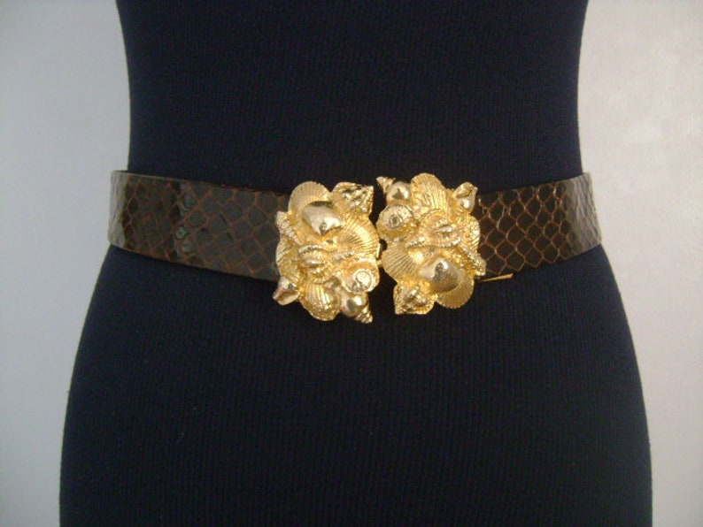 May include: A brown leather belt with a large gold buckle featuring a seashell design.
