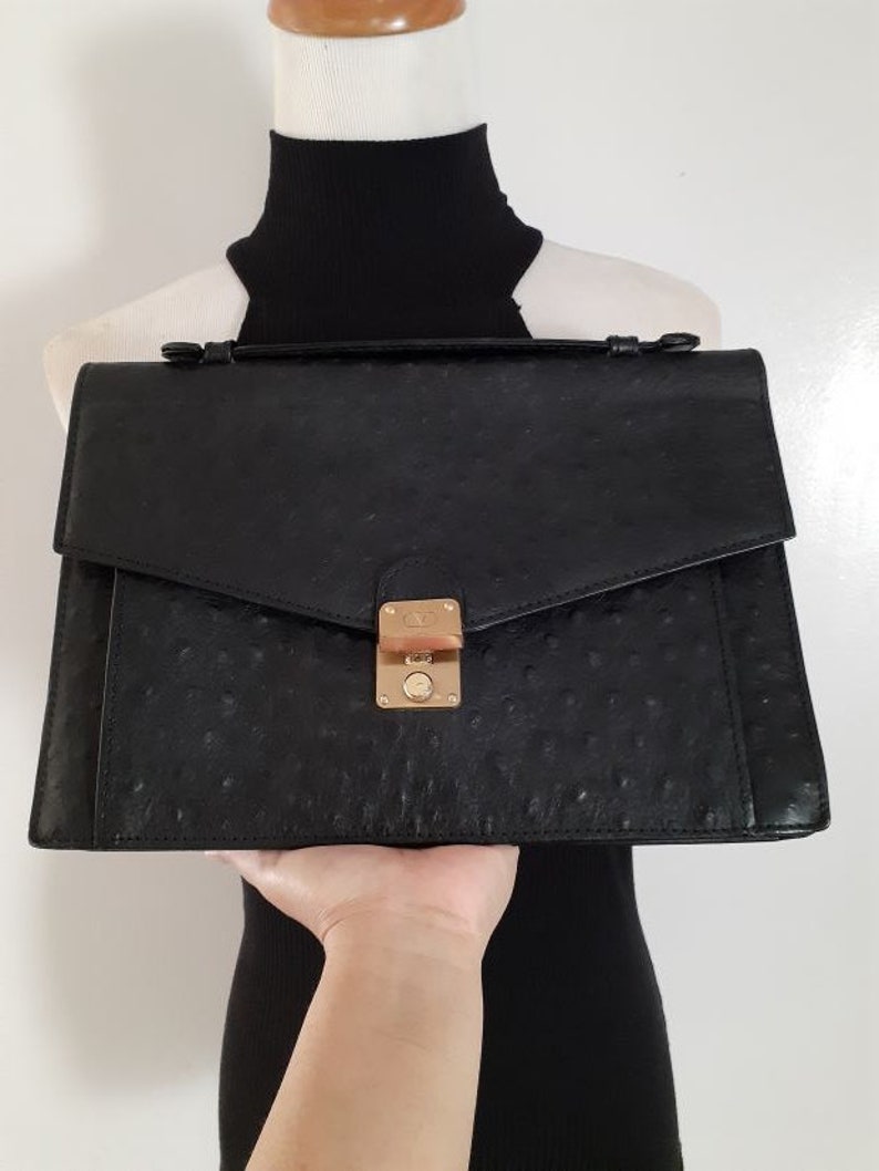 May include: A black ostrich leather briefcase with a gold clasp and a top handle.