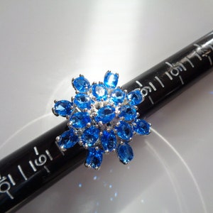 May include: A silver ring with a cluster of blue topaz stones set in a starburst design.