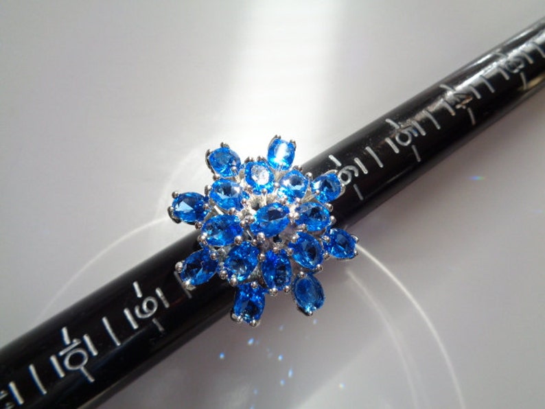 May include: A silver ring with a cluster of blue topaz stones set in a starburst design.