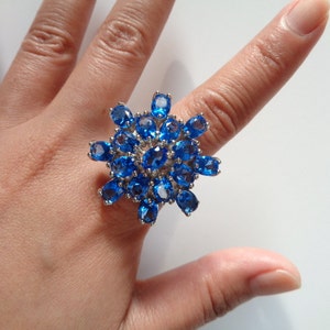 May include: A silver ring with a large blue gemstone cluster in the shape of a flower.