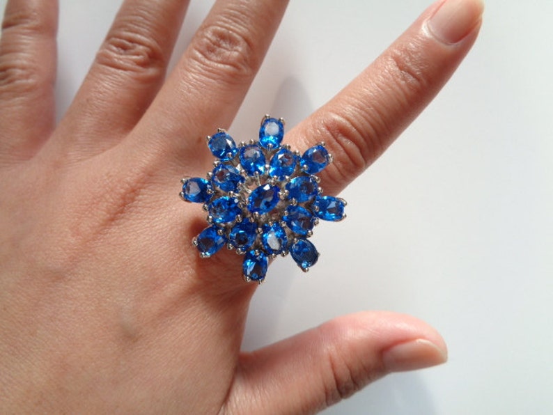 May include: A silver ring with a large blue gemstone cluster in the shape of a flower.