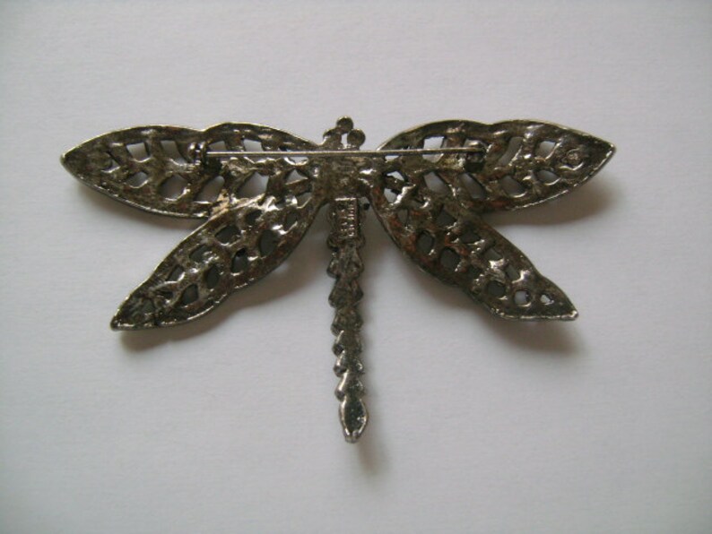 May include: Silver-toned dragonfly brooch with intricate cut-out details. The brooch has a pin and catch closure on the back.