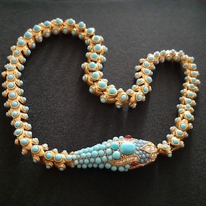 May include: A gold snake necklace with turquoise and clear stones. The snake's head is detailed with a red stone for the eye.