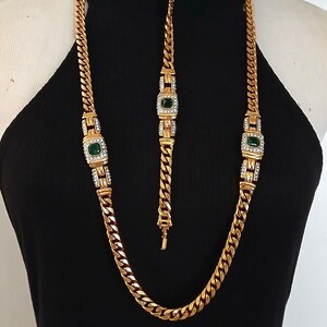 May include: Gold-toned necklace and bracelet set. The necklace and bracelet feature a curb chain design with emerald-green and clear crystal accents. The jewelry is displayed on a black mannequin.