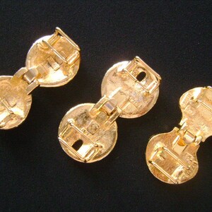 May include: Three gold-toned metal clasps with a hinged design. Each clasp has two round sections connected by a hinge.