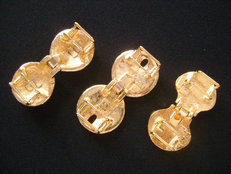 May include: Three gold-toned metal clasps with a hinged design. Each clasp has two round sections connected by a hinge.