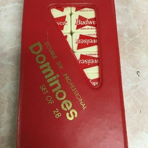 May include: A red, rectangular box with gold lettering that reads "Dominoes Double Six Professional Set of 28". The box has a clear plastic window that shows a set of dominoes with the Budweiser logo.
