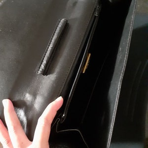 May include: Black leather handbag with a zipper closure and a gold-colored metal accent. The bag is open and the inside is visible.