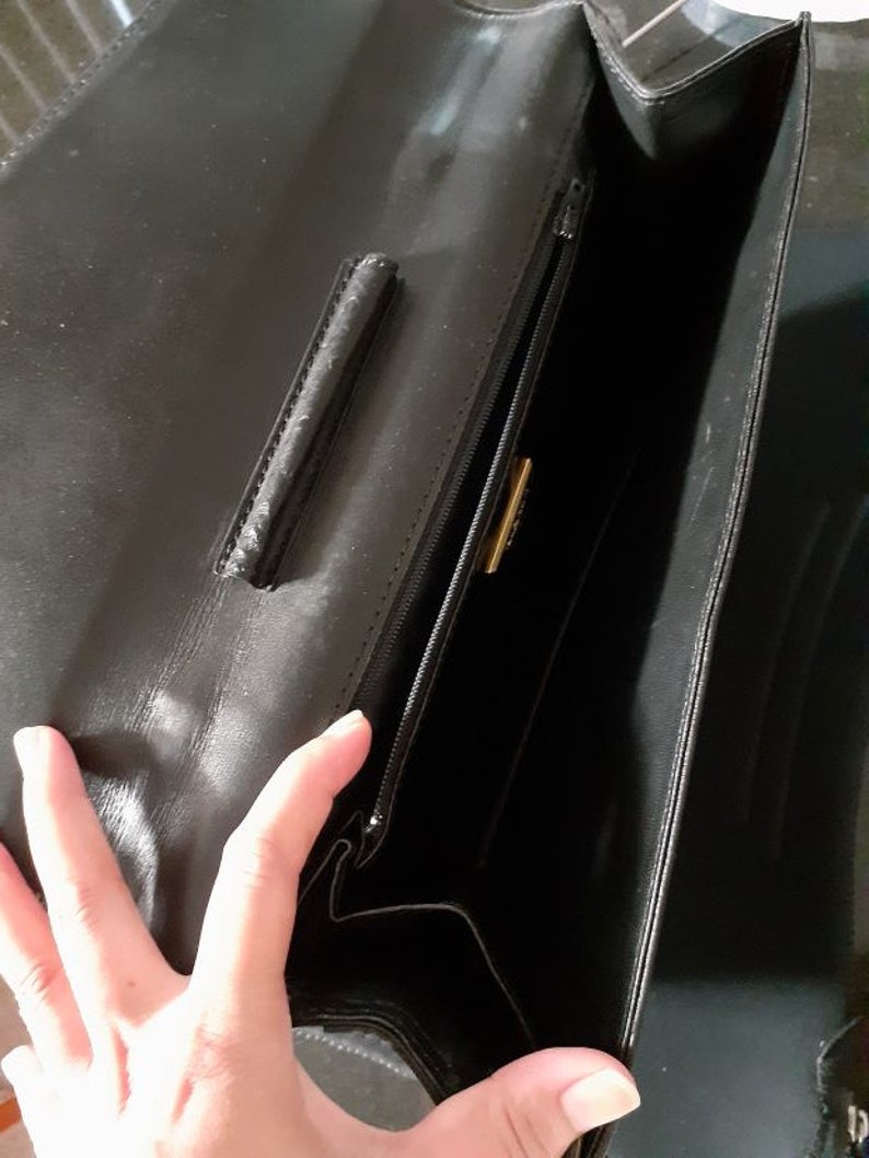 May include: Black leather handbag with a zipper closure and a gold-colored metal accent. The bag is open and the inside is visible.