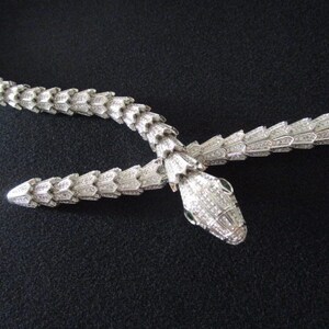 Op de afbeelding: Een zilveren slangenketting met een diamantbezette ontwerp. De kop van de slang is naar voren gericht met de mond open.