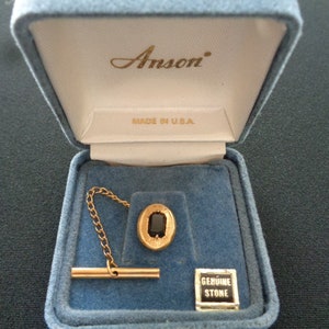 Peut inclure: Un fermoir de cravate en or avec une pierre précieuse noire dans un coffret en velours bleu. Le coffret porte les inscriptions "Anson" et "Made in U.S.A.". Le coffret comporte également une petite étiquette indiquant "Genuine Stone".