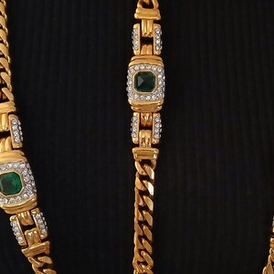 May include: Gold-toned necklace and bracelet set. The necklace and bracelet feature a curb chain design with rectangular links. Each link has a square emerald-green stone surrounded by clear crystals.