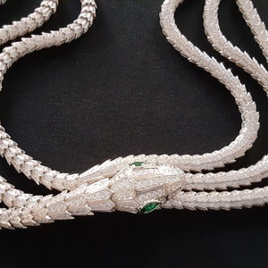 Peut inclure: Un collier en argent avec une cha&icirc;ne en forme de serpent et un pendentif t&ecirc;te de serpent. La t&ecirc;te de serpent est incrust&eacute;e de pierres claires et a des yeux verts.