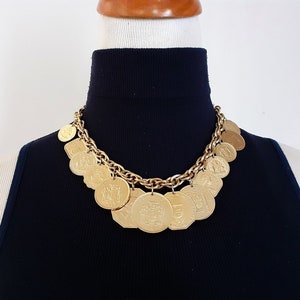 May include: A gold chain necklace with multiple gold coin charms. The coins have various designs and are attached to the chain with jump rings.