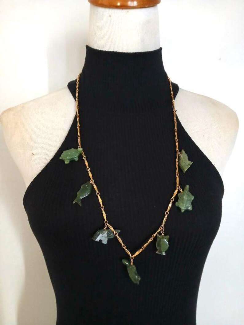 May include: A gold chain necklace with green jade animal charms. The charms include a turtle, fish, owl, and other animals.