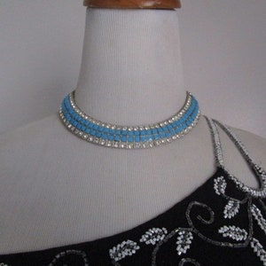 Puede incluir: Un collar gargantilla de pedrer&iacute;a azul y plata en un maniqu&iacute; blanco. El collar tiene tres filas de pedrer&iacute;a cuadrada.