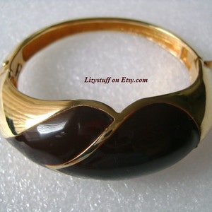 May include: A gold-tone bangle bracelet with a black enamel design. The bracelet has a hinged clasp.