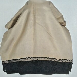 May include: A beige fabric scarf with a black lace trim. The lace trim has a floral design.