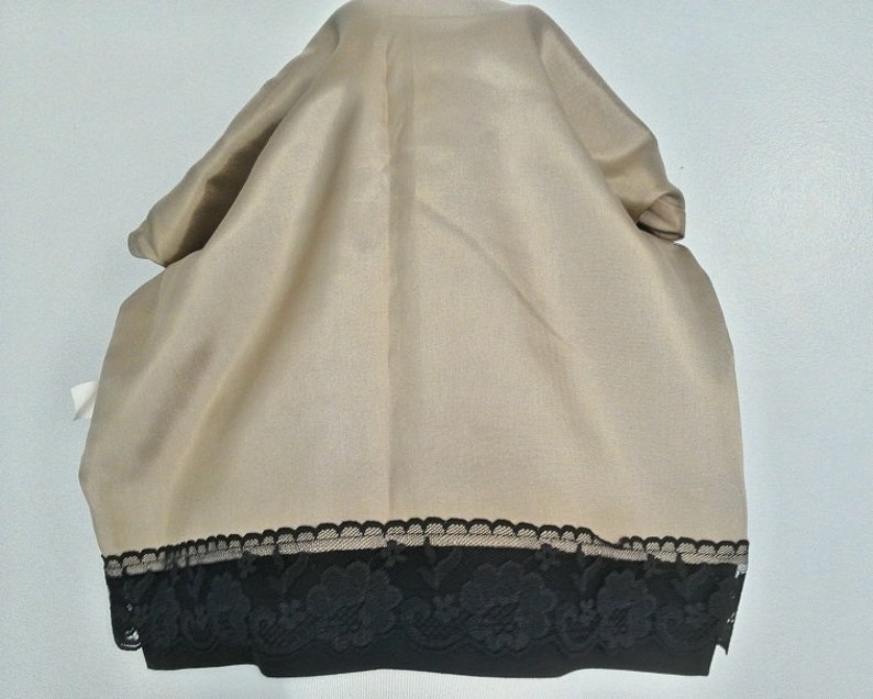 May include: A beige fabric scarf with a black lace trim. The lace trim has a floral design.