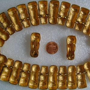 May include: A gold-tone necklace with a repeating pattern of linked rectangular shapes. The necklace is paired with matching gold-tone clip-on earrings.