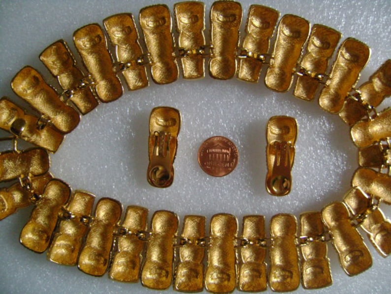 May include: A gold-tone necklace with a repeating pattern of linked rectangular shapes. The necklace is paired with matching gold-tone clip-on earrings.