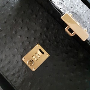 May include: Black leather handbag with a gold combination lock and a gold clasp. The lock has the numbers 5654, 7663.