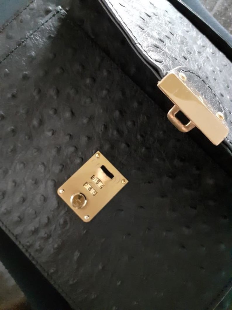 May include: Black leather handbag with a gold combination lock and a gold clasp. The lock has the numbers 5654, 7663.