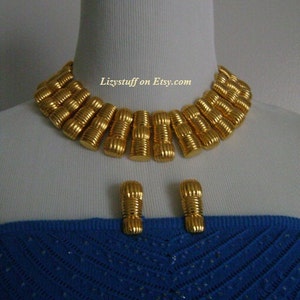 May include: A gold-tone statement necklace and matching earrings. The necklace is made of a series of linked, ridged, gold-tone cylinders. The earrings are simple, gold-tone cylinders.  Lizystuff on Etsy.com