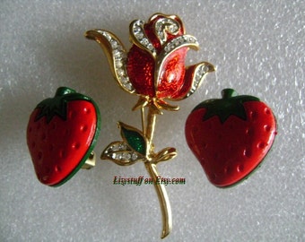 May include: A set of three vintage costume jewelry pieces featuring a red rose brooch with rhinestones and two red strawberry earrings with green leaves.