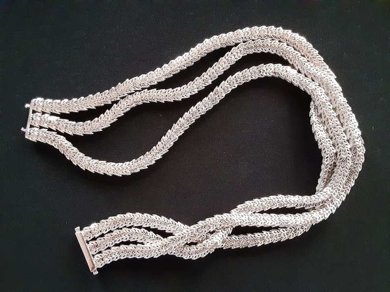 Peut inclure: Un collier en argent avec un design &agrave; trois brins. Chaque brin est compos&eacute; de petits maillons entrelac&eacute;s qui cr&eacute;ent un motif d&eacute;licat et complexe.
