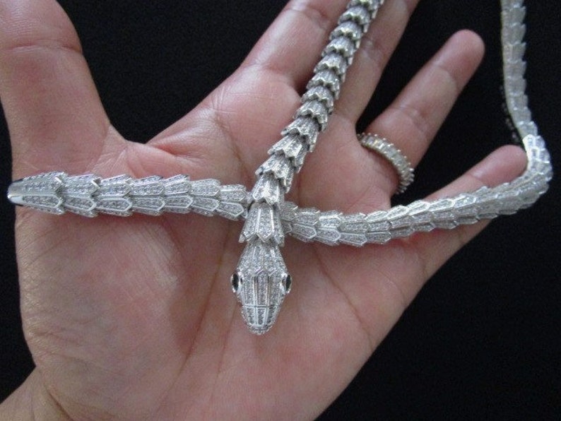 Op de afbeelding: Een zilveren slangenketting met een diamant-achtige afwerking. De ketting is in de vorm van een slang met zijn kop omhoog en zijn staart om de nek gewikkeld.
